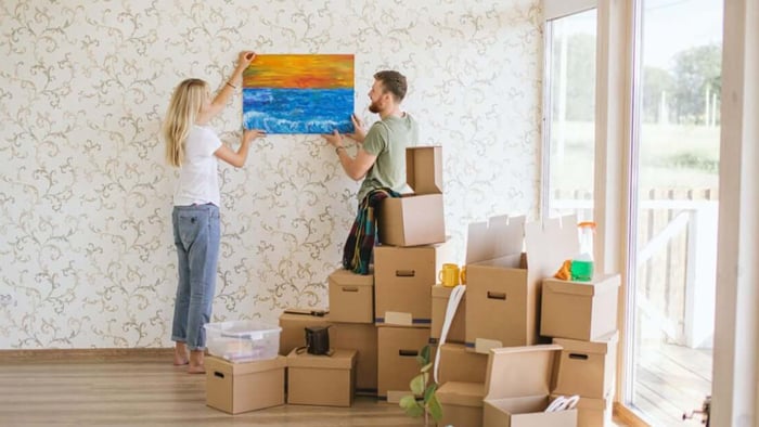 Couple hanging picture on wall in new home