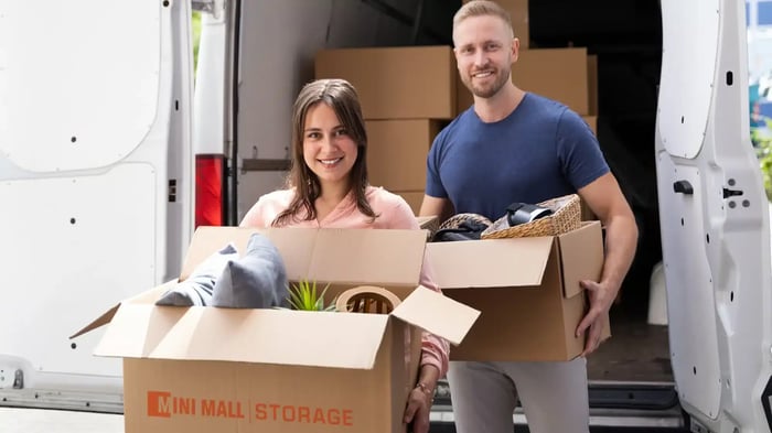 A couple holding Mini Mall Storage-branded moving boxes as they exit a moving truck
