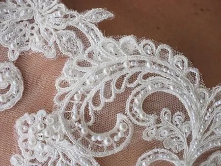 Alencon or French Embroidered Lace is immensely popular as a bridal fabric for making wedding gowns and veils. This beautiful lace has a net background and raised motifs with beads and cords embellishing it. Basically, it is Chantilly lace with a raised design.