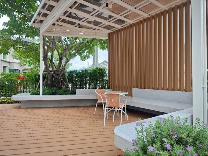 ต่อเนื่องจากห้องนั่งเล่นด้านในออกมาคือชานบ้านไม้เทียมที่บริษัท Interior Design ออกแบบให้เชื่อมกับผนังและหน้าต่างกระจกบานใหญ่ ซึ่งมีข้อดีคือด้านในบ้านจะได้รับแสงจากธรรมชาติอย่างเต็มที่