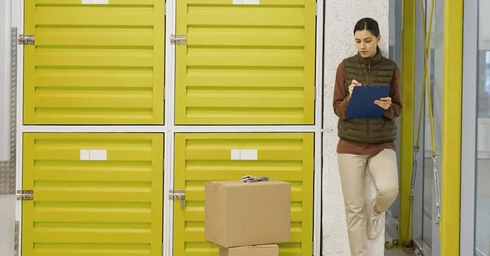 Woman checking off boxes on a clipboard outside yellow storage lockers at a storage facility