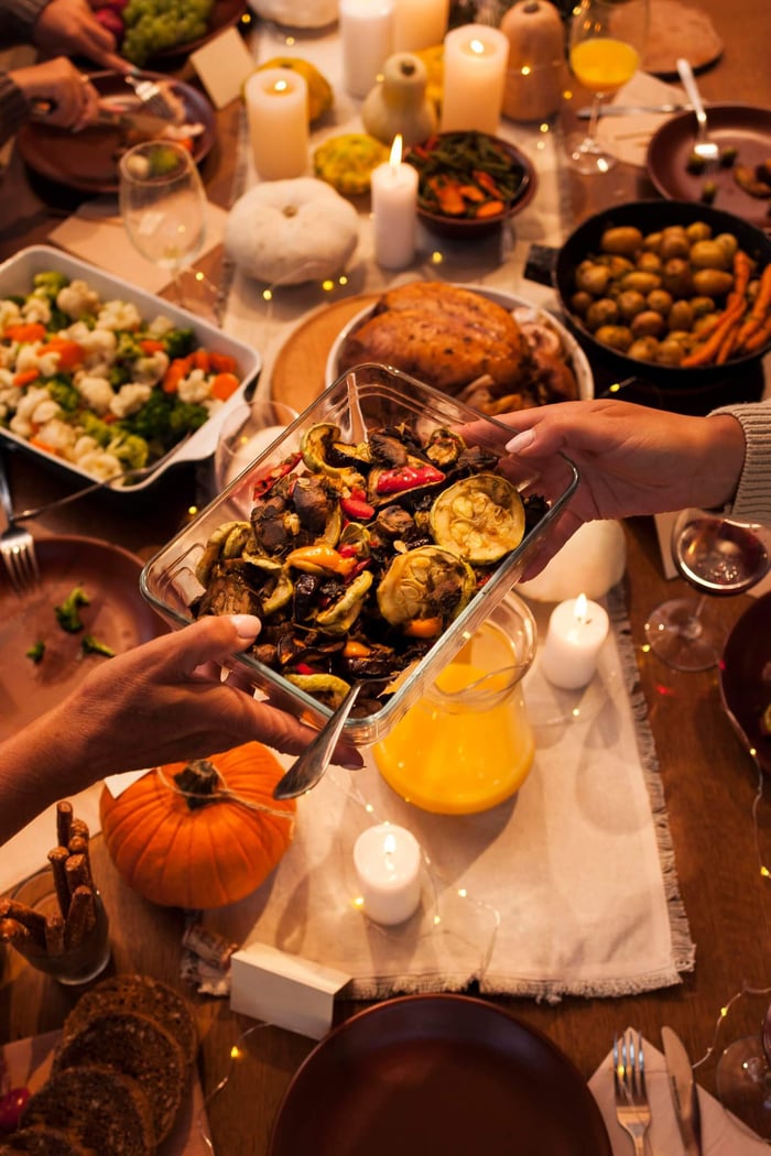high angle view of two hands passing dishes over a set table at friendsgiving dinner