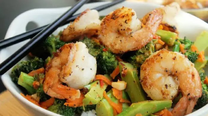 a bowl of shrimp and vegetables on a bed of rice with chopsticks