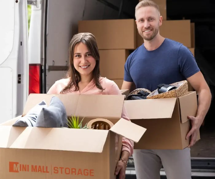 a couple holding Mini Mall Storage-branded moving boxes as they exit a moving truck