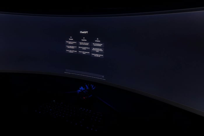 Close-up of a dark room with a curved monitor showing the ChatGPT interface on screen.