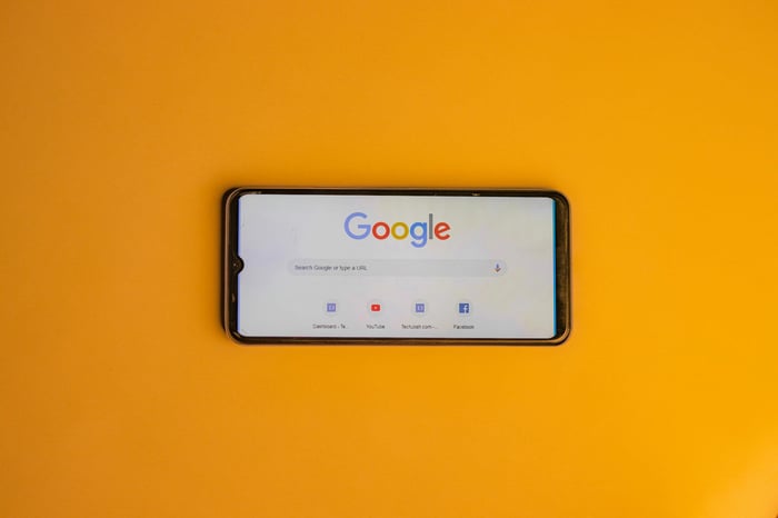 Smartphone displaying Google search page on a vibrant yellow background.