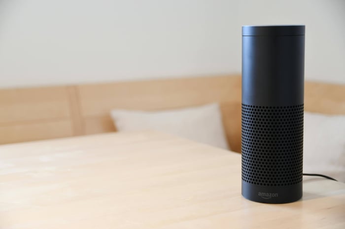 A black smart speaker resting on a light-colored wooden table in a cozy indoor setting.