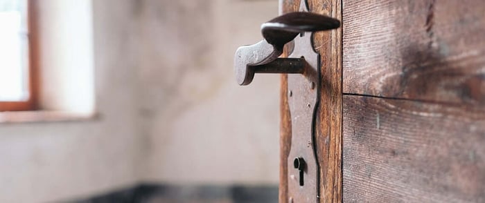 Inside of a fixer upper-home shows an open door with a door handle in focus, showing the interior of the room blurred out in the background.