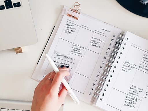 Woman writing in daily planner with a laptop nearby