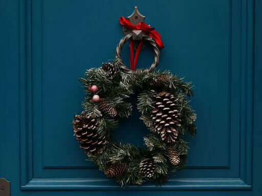 A pinecone and pine wreath hanging on a blue door
