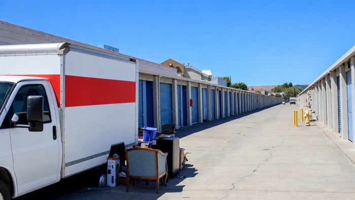 Moving truck parked beside drive-up storage units with furniture and household items ready for loading