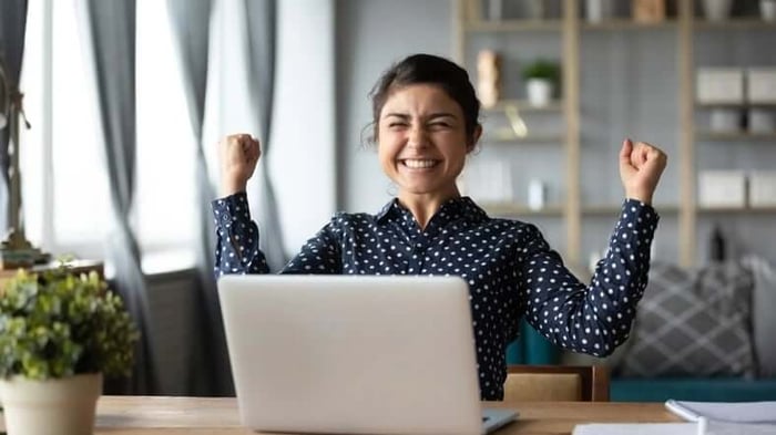 A woman sitting at her laptop with her fists raised.