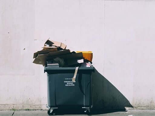 A recycling bin against a white building filled with cardboard
